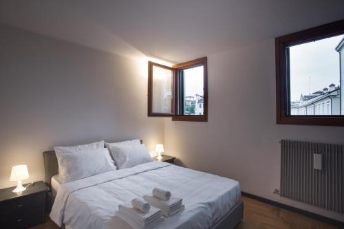 una camera da letto con un grande letto bianco con due finestre di Filodrammatici Loft by Welc(H)ome a Treviso