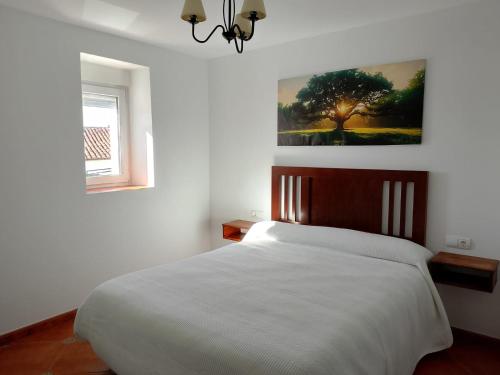 a bedroom with a white bed with a painting on the wall at Casa La Piedra in Constantina