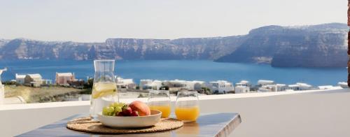 a table with two glasses of juice and a bowl of fruit at Aelia Suites Akrotiri, Santorini in Akrotiri