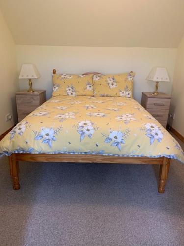 a bed with a yellow comforter and two night stands at Sineag's Cottage in Pollachar