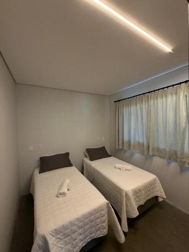 two beds in a small room with a window at Pitaya Apart Hotel in Garopaba