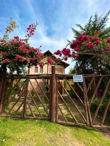 a wooden gate in front of a house with pink flowers at Chalé no coração de Penedo - Pet Friendly in Itatiaia