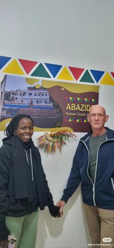 a man and a woman holding hands in front of a sign at ABAZIDO Nubian Guest House in Aswan