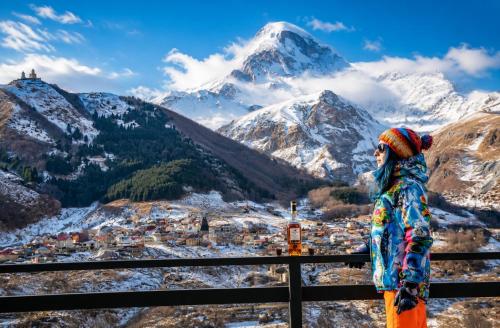 a woman standing on a fence looking at a snowy mountain at Old District View Hotel kazbegi in Kazbegi