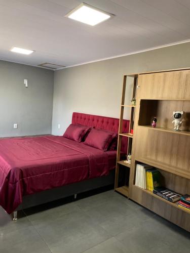 a bedroom with a red bed and a book shelf at suíte perto da praia in Imbituba