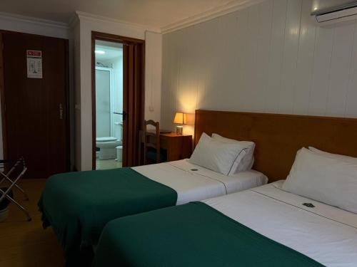 a hotel room with two beds and a bathroom at Hospedaria Insular in Ponta Delgada