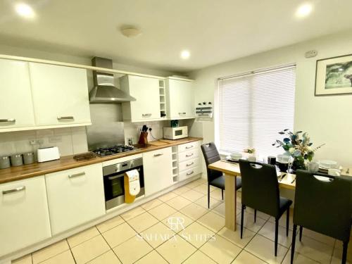 a kitchen with white cabinets and a table and chairs at 4 Bed House with Driveway Parking for 2 Cars - Rugby - Sleeps 10! Perfect for groups! in Rugby