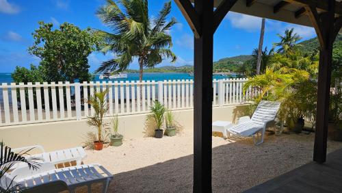 a porch with white chairs and palm trees and the ocean at Bibi Beach Sunrise in La Trinité