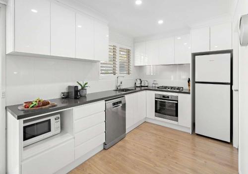 a kitchen with white cabinets and stainless steel appliances at Flinders Hideaway in Shellharbour