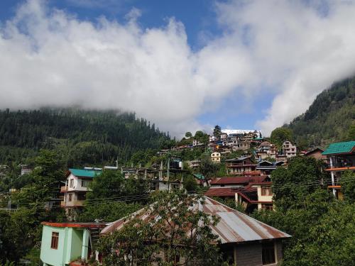a village on a hill with houses and trees at Nirvana Stays and Cafe in Manāli