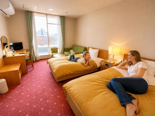 two women laying on beds in a hotel room at Hotel Lavenir in Biei