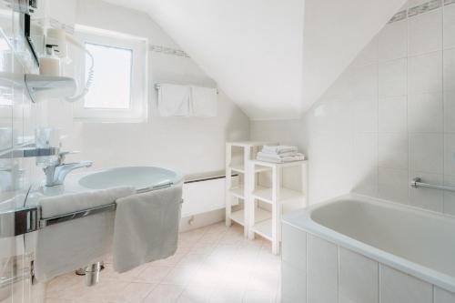 a white bathroom with a sink and a tub at Inselhotel Faakersee in Faak am See