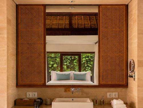 a bathroom with a sink and a window with a bed at REVĪVŌ Wellness Resort Nusa Dua Bali in Nusa Dua
