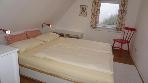 a bed in a room with a red chair and a window at Gut Settin am See - Ferienhäuser in Settin