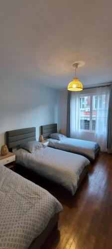 two beds in a bedroom with a window and a chandelier at Dieppe plage à 2min à pied in Dieppe