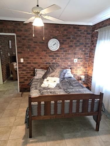 a bed in a room with a brick wall and a clock at Siësta Guesthouse in Modimolle