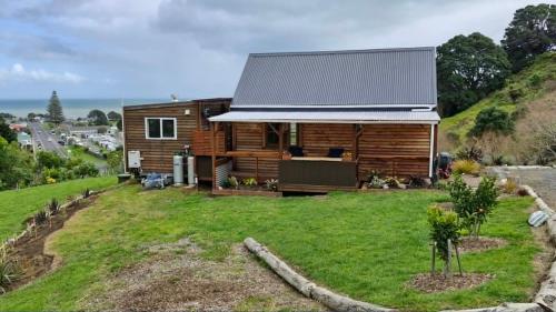 a log cabin on a hill with a grass yard at Kōtare Cabin, Thames Coast in Tapu