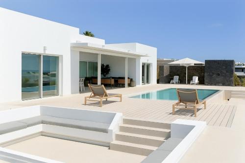 a white villa with a swimming pool and two chairs at Villa Ainé Luxury Villa, Sea Views, Heated pool in Puerto Calero