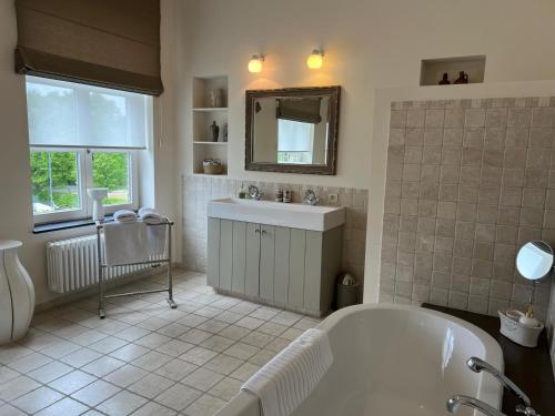 ein Badezimmer mit Badewanne, Waschbecken und Spiegel in der Unterkunft De Pastory Peer in Grote-Brogel