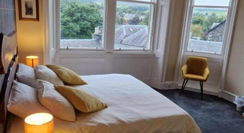 a bedroom with a bed with two windows and a chair at Neidpath inn in Peebles