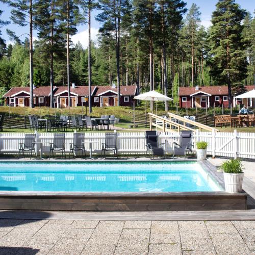 a swimming pool with chairs and a house in the background at Hotell Moskogen in Leksand