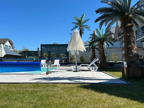 a pool with a white umbrella and chairs and palm trees at Sunny Baltic in Jarosławiec