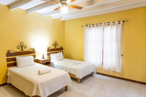 two beds in a room with yellow walls and a window at Hosteria Suiza in Ica