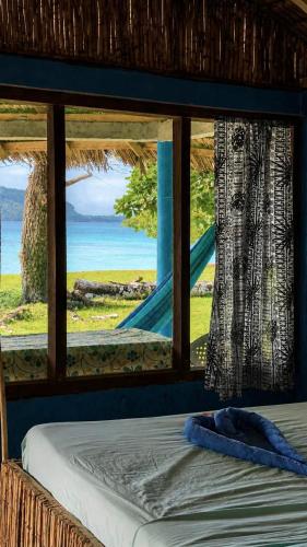 a bed with a view of the ocean from a window at Lonnoc ocean view beach bungalows in Hog Harbour