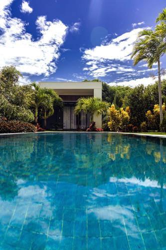 a large swimming pool with blue water in front of a house at Villa Egeu Praia da Pipa in Pipa
