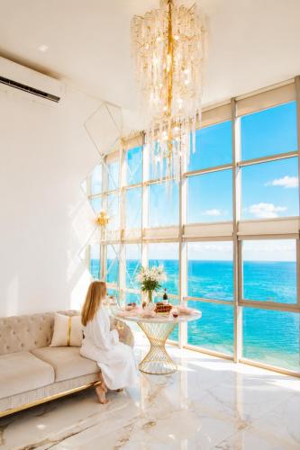 a woman sitting on a couch in a room with a large window at Penthouse Panorama Luxury Sea View Premium Stay in Batumi in Batumi