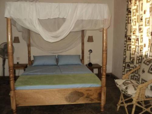 1 dormitorio con 1 cama con dosel y 1 silla en Coast Sun Gardens Cottage en Msambweni