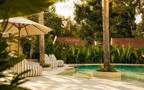 a pool with white chairs and an umbrella and trees at Loku Kedungu - Boutique Resort in Tanah Lot