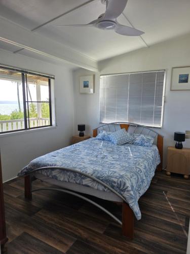a bedroom with a bed with a blue comforter and two windows at The Crab Shack in Boonooroo