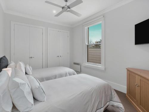 a white bedroom with two beds and a flat screen tv at The Scoop in Queenscliff