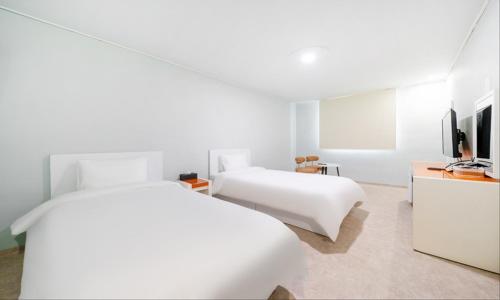 two beds in a white room with a tv at Taean Manripo Feel Hotel in Taean