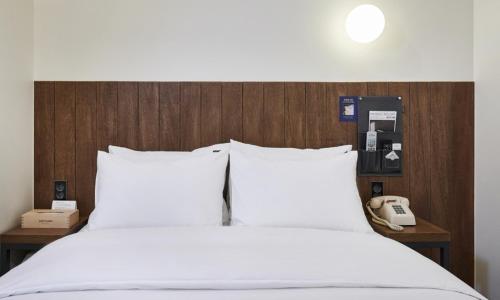 a bed with white sheets and a phone on a wall at JustSleep Namyangju Dasan in Namyangju