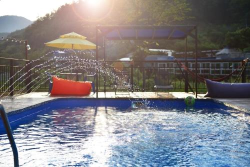 a swimming pool with an umbrella and a water fountain at Gapyeong Gratia glamping in Gapyeong