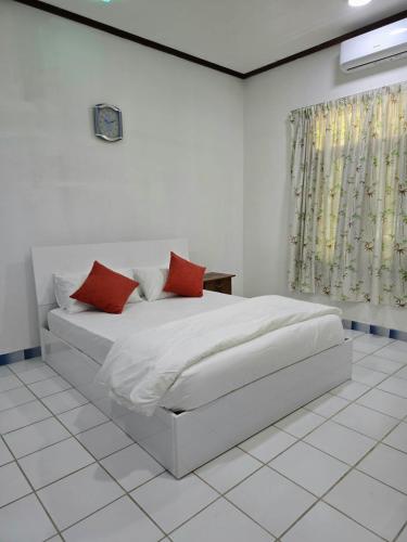 ein weißes Schlafzimmer mit einem Bett und zwei roten Kissen in der Unterkunft Beevaa Inn in Fuvahmulah