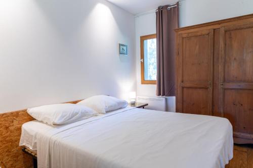 a bedroom with a white bed with a wooden cabinet at Le Refuge in Patrimonio