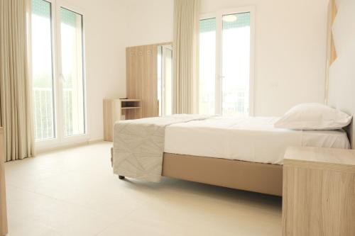 a white bedroom with a bed and large windows at Hotel Mariblu in Rimini