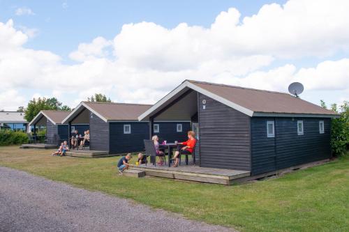 a family sitting at a table outside of a tiny house at Frederikshavn Nordstrand Camping & Cottages in Frederikshavn