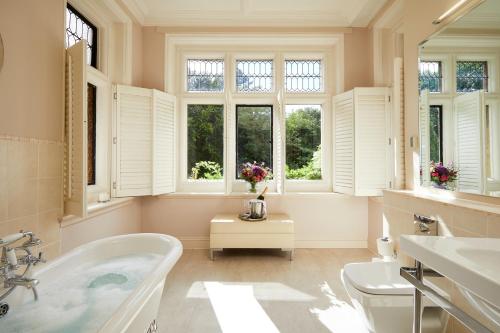 a bathroom with a tub and a toilet and windows at Macdonald Frimley Hall Hotel & Spa in Camberley