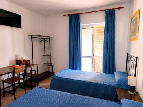 a bedroom with two beds and a desk and a window at Hostal Fantoni in Cádiz