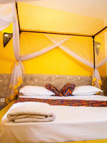 a bed with a yellow wall and two towels on it at La Maison Chocolat in Nianing