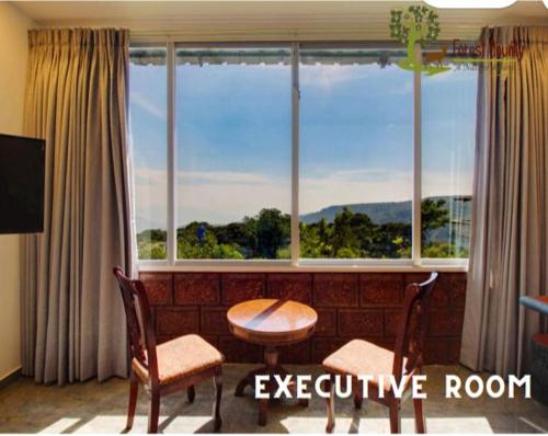 a living room with a table and chairs and a large window at Forest County Resort Mahabaleshwar in Mahabaleshwar
