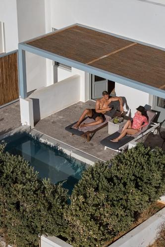 two men sitting on lounge chairs next to a swimming pool at Paros Cape Suites in Naousa