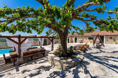 a tree and benches in front of a house at My Dalmatia - Hilltop Paradise with private pool, sauna and Jacuzzi in Kula Atlagić