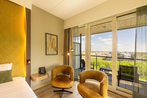 a hotel room with a bed and two chairs and a balcony at Strandhotel Het Hoge Duin in Wijk aan Zee