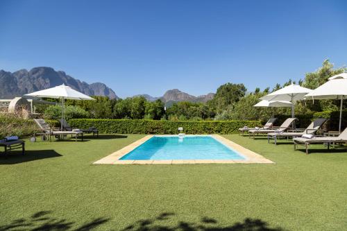 a swimming pool with lawn chairs and umbrellas at La Cabriere Country House in Franschhoek