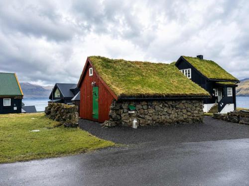 a red barn with a grass roof on a field at Traditional Cabin with Sea View in Stykkið